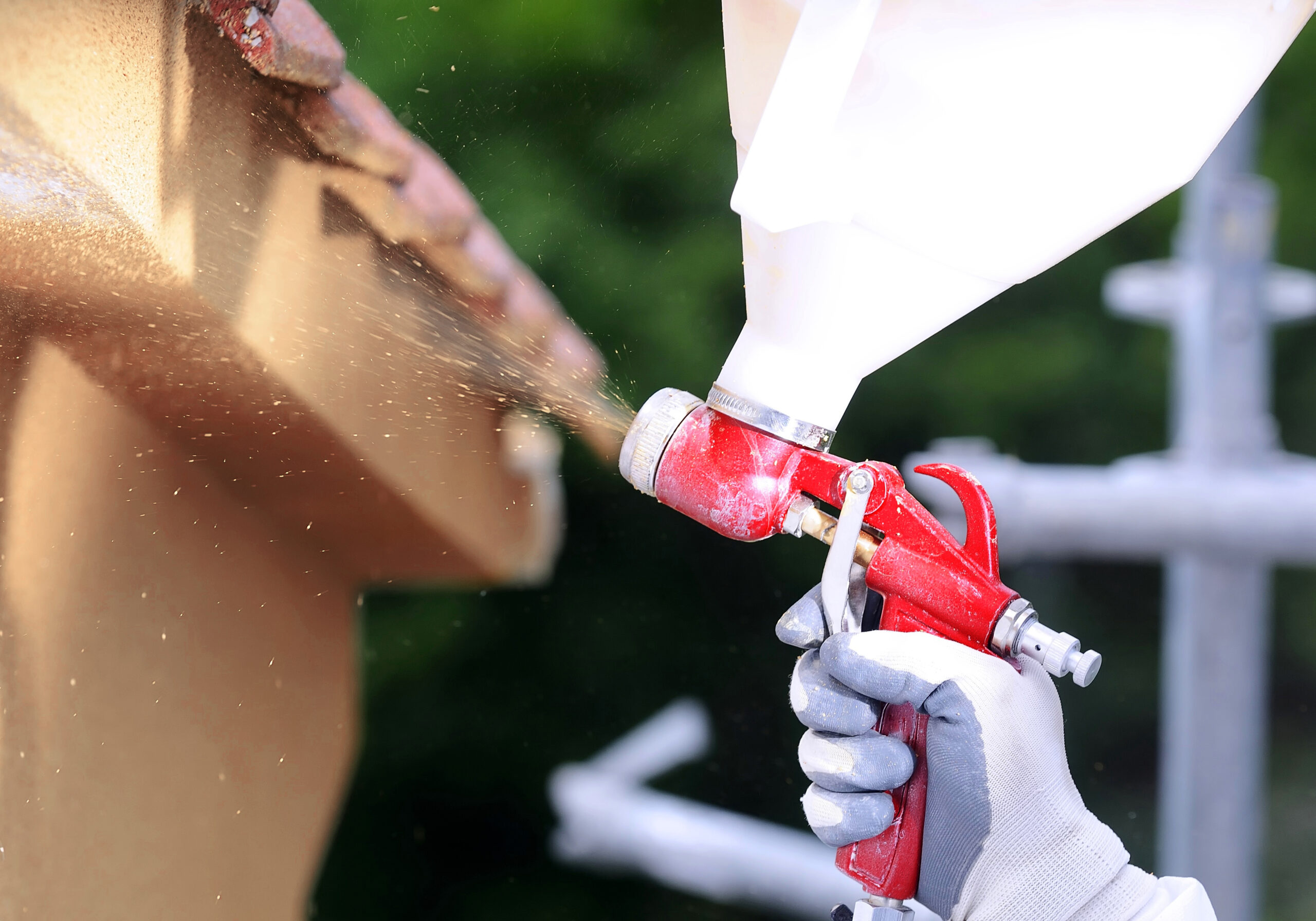 A person wearing a white glove applies cork spray to a house using a spray can, showcasing a home improvement project.