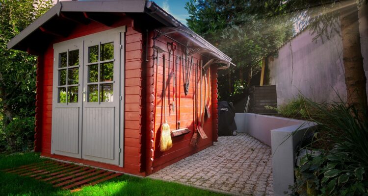 A vibrant red shed with a door and a window, surrounded by greenery.